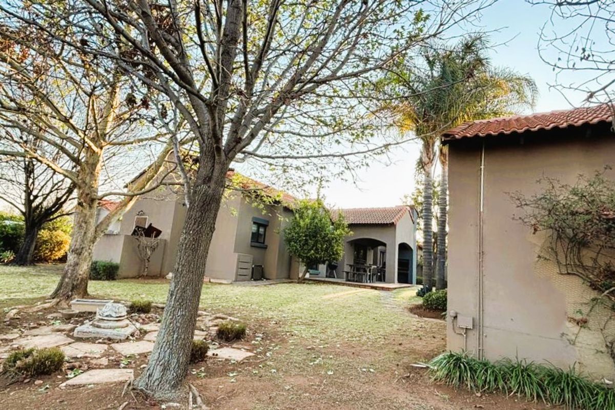 Rear view of the townhouse featuring a covered patio, terracotta roof tiles, and a spacious garden area with mature trees.