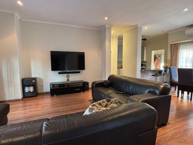 Spacious open-plan living and dining area featuring laminate flooring, recessed lighting, and an air conditioning unit, with direct access to the patio.