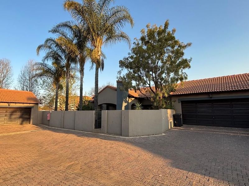Front exterior view of a townhouse featuring a paved driveway, perimeter wall, and both single and double garage access points.