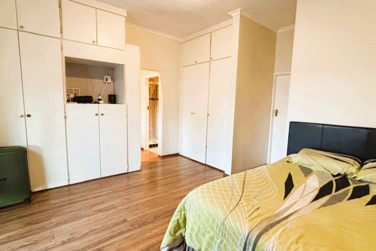 A bedroom featuring extensive built-in cupboard storage, laminate flooring, and neutral wall finishes, with an adjoining doorway leading to an en-suite bathroom.