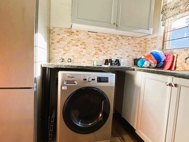 A functional laundry area featuring built-in cabinetry, stone countertops, a mosaic tile backsplash, and a stainless steel sink.