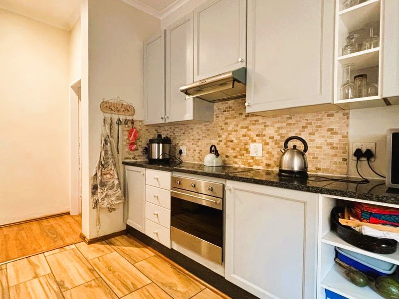 A functional kitchen featuring light-toned cabinetry, granite countertops, a mosaic tile backsplash, and integrated stainless steel appliances with durable ceramic floor tiling.