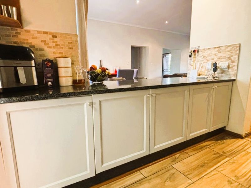 A functional kitchen featuring white shaker-style cabinetry, a dark granite breakfast bar, and a decorative tiled backsplash, opening into the adjacent living area.