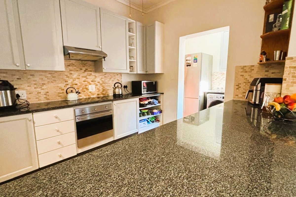 A functional kitchen featuring granite countertops, built-in oven, extractor fan, and ample cabinetry, with an adjacent scullery area visible.