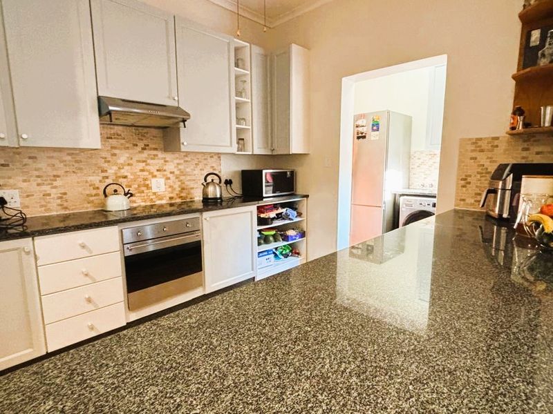 A functional kitchen featuring granite countertops, built-in oven, extractor fan, and ample cabinetry, with an adjacent scullery area visible.