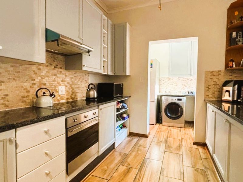 A functional kitchen featuring shaker-style cabinetry, granite countertops, a built-in oven, and a tiled backsplash, with an adjoining scullery area.