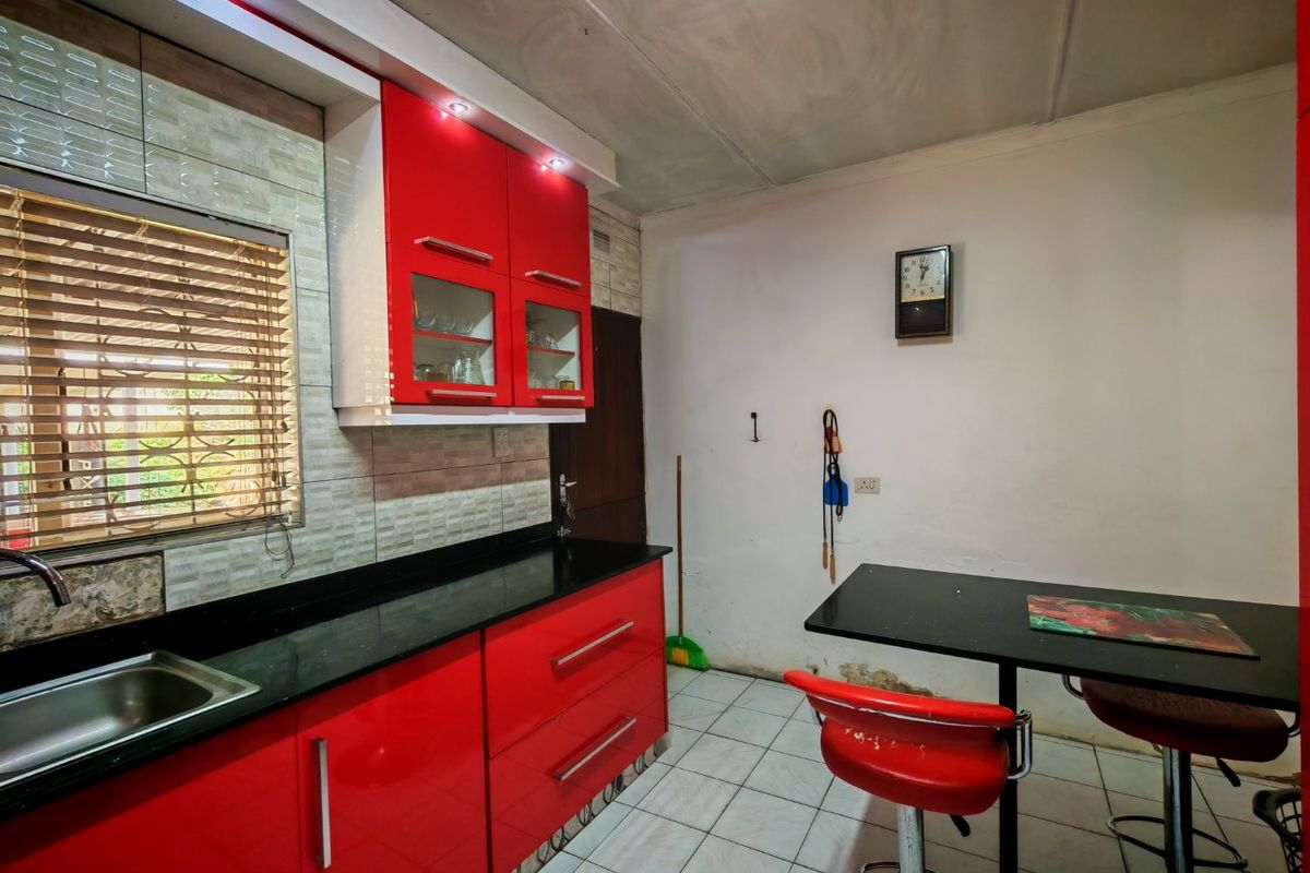 Compact kitchen featuring high-gloss red cabinetry, black granite countertops, and tiled flooring, requiring some cosmetic wall repairs to restore its finish.