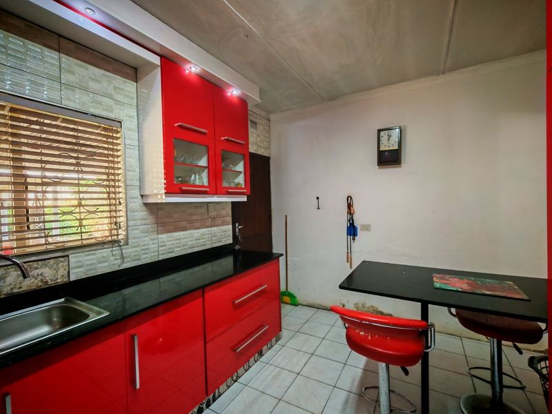 Compact kitchen featuring high-gloss red cabinetry, black granite countertops, and tiled flooring, requiring some cosmetic wall repairs to restore its finish.