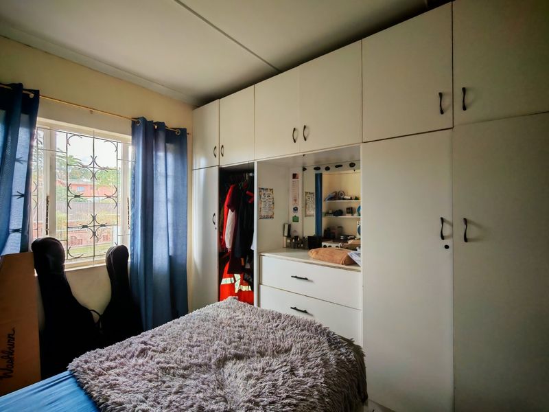 A bedroom featuring extensive floor-to-ceiling built-in cupboards with an integrated vanity area and security bars on the window.
