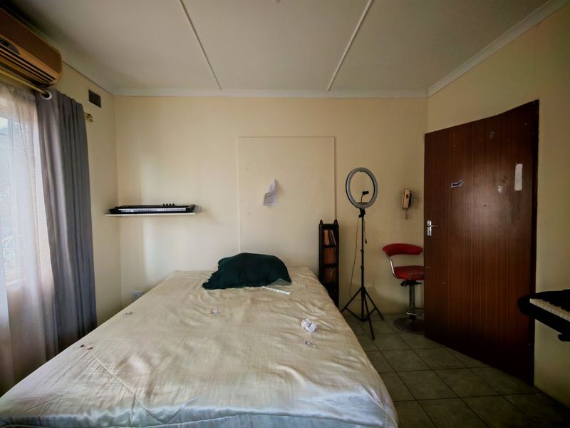 A functional bedroom featuring tiled flooring and an integrated air conditioning unit, offering a neutral base for potential interior updates.