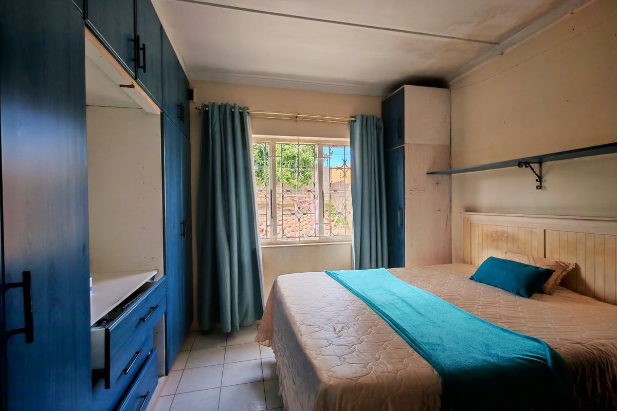 A bedroom featuring built-in cupboards, tiled flooring, and a window with security bars, offering a functional space with potential for cosmetic updates.