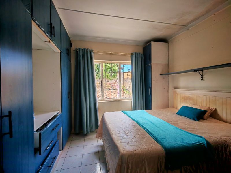 A bedroom featuring built-in cupboards, tiled flooring, and a window with security bars, offering a functional space with potential for cosmetic updates.