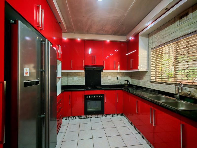 Modern kitchen featuring high-gloss red cabinetry, black granite countertops, built-in oven, and tiled flooring, offering a bold and functional culinary space.