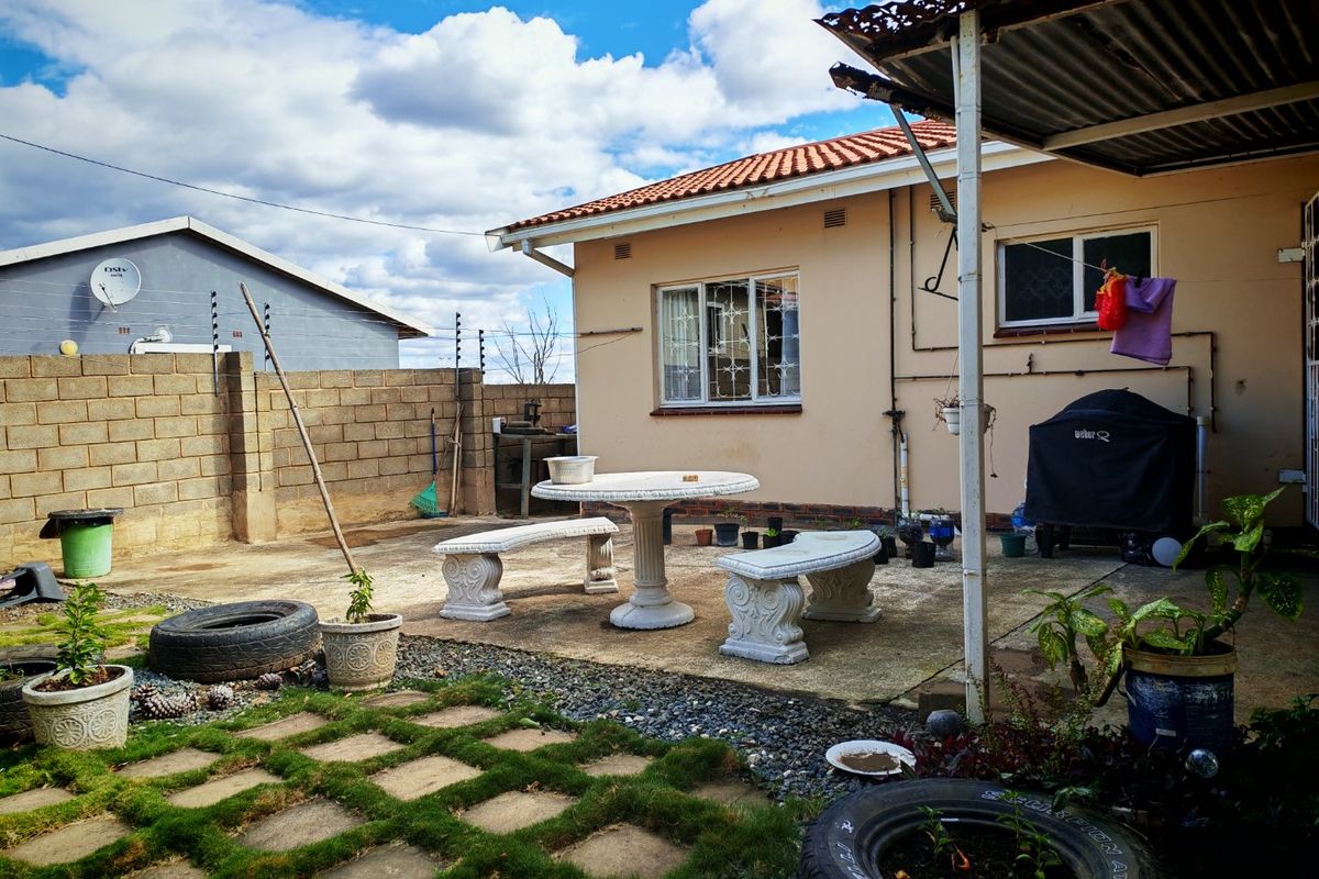 Rear exterior view of the house featuring a concrete patio area, brick boundary wall with electric fencing, and a covered outdoor space.