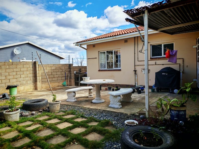 Rear exterior view of the house featuring a concrete patio area, brick boundary wall with electric fencing, and a covered outdoor space.
