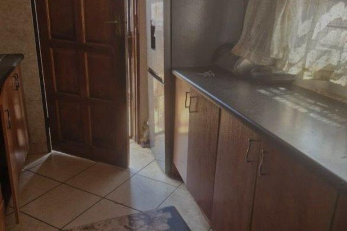 A dated kitchen featuring timber cabinetry, dark laminate countertops, and ceramic floor tiles, with direct access to an exterior door.