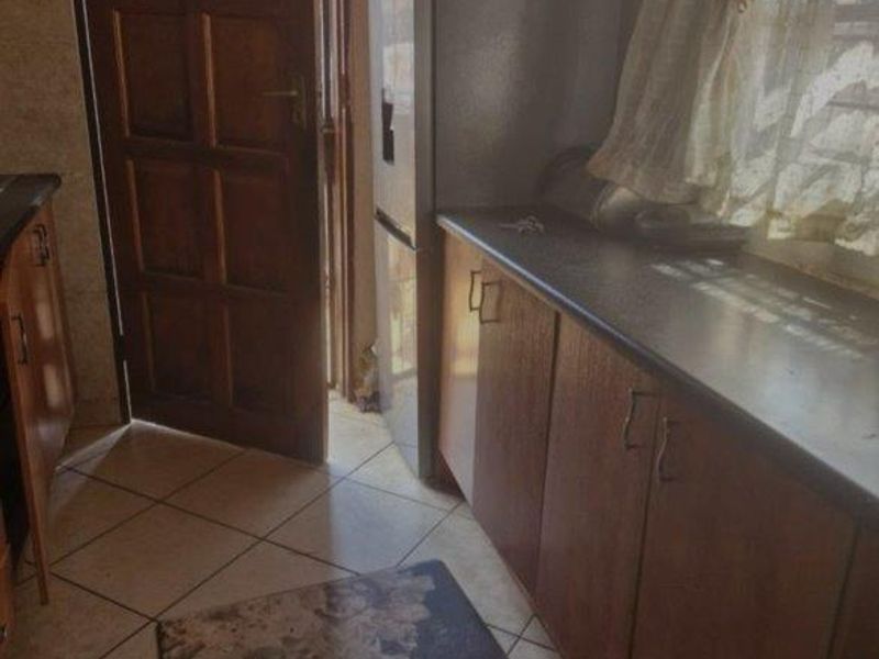 A dated kitchen featuring timber cabinetry, dark laminate countertops, and ceramic floor tiles, with direct access to an exterior door.