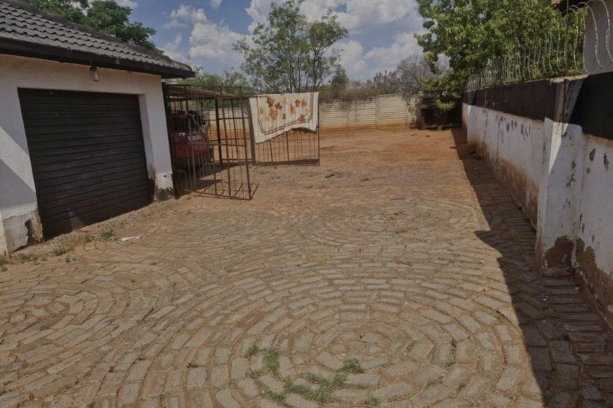 Rear exterior area featuring a paved driveway, perimeter wall with security fencing, and access to a garage.