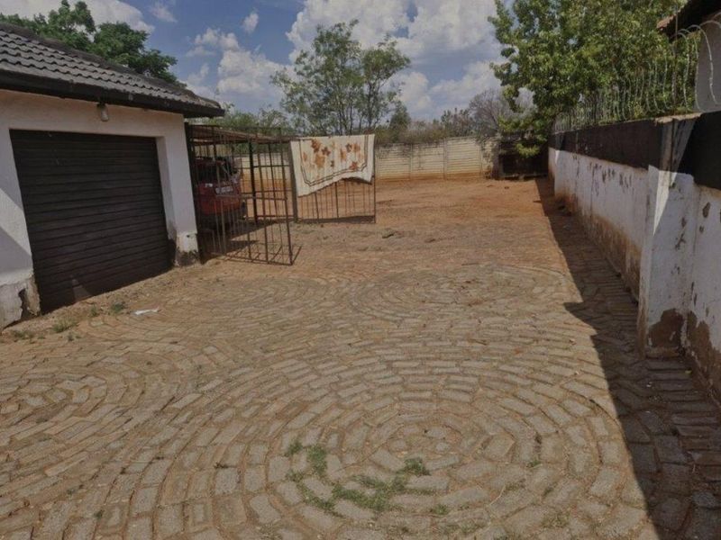 Rear exterior area featuring a paved driveway, perimeter wall with security fencing, and access to a garage.