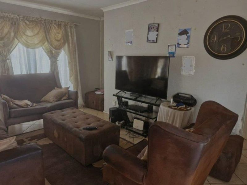 A living room featuring tiled flooring and curtain rails, showing signs of wear on the wall surfaces.