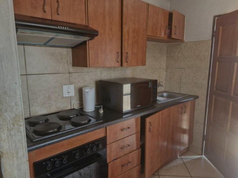 A compact kitchen featuring wooden cabinetry, a built-in oven with electric hob, extractor fan, and tiled backsplash, requiring some maintenance and cosmetic updates.