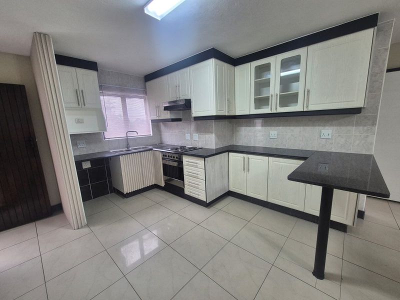 A clean, functional kitchen featuring white cabinetry, dark granite countertops, a breakfast bar, and built-in appliances including an oven and extractor fan.