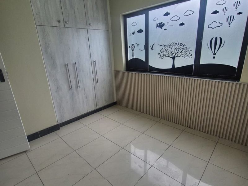 A bright, empty bedroom featuring modern built-in cupboards, neutral tiled flooring, and decorative window film, offering a clean and versatile living space.