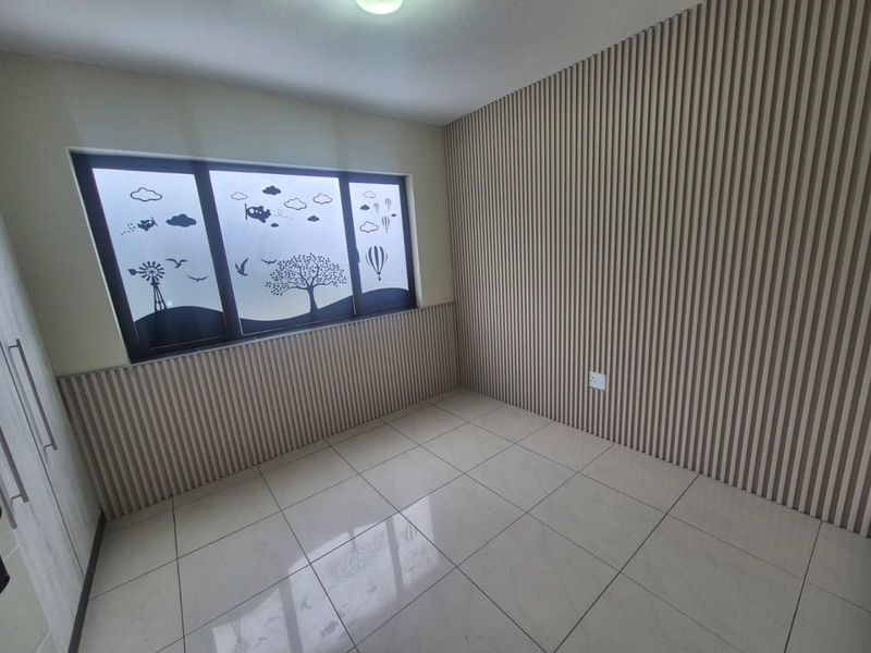 A bright, empty bedroom featuring modern slatted wood wall paneling, neutral tiled flooring, and a built-in wardrobe with a window featuring decorative film.