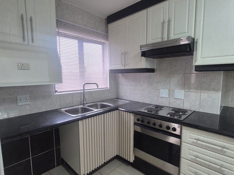 A clean, functional kitchen featuring white cabinetry, black granite countertops, built-in oven, electric hob, and tiled finishes throughout.