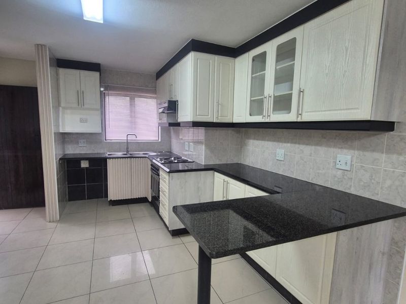 A clean, functional kitchen featuring granite countertops, ample built-in cabinetry, a breakfast bar, and tiled flooring, offering a neutral and well-maintained workspace.