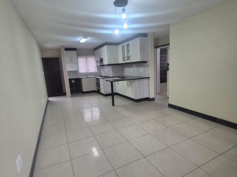 An open-plan living and kitchen area featuring neutral tiled flooring, modern built-in cabinetry, a kitchen island, and integrated cooking appliances.