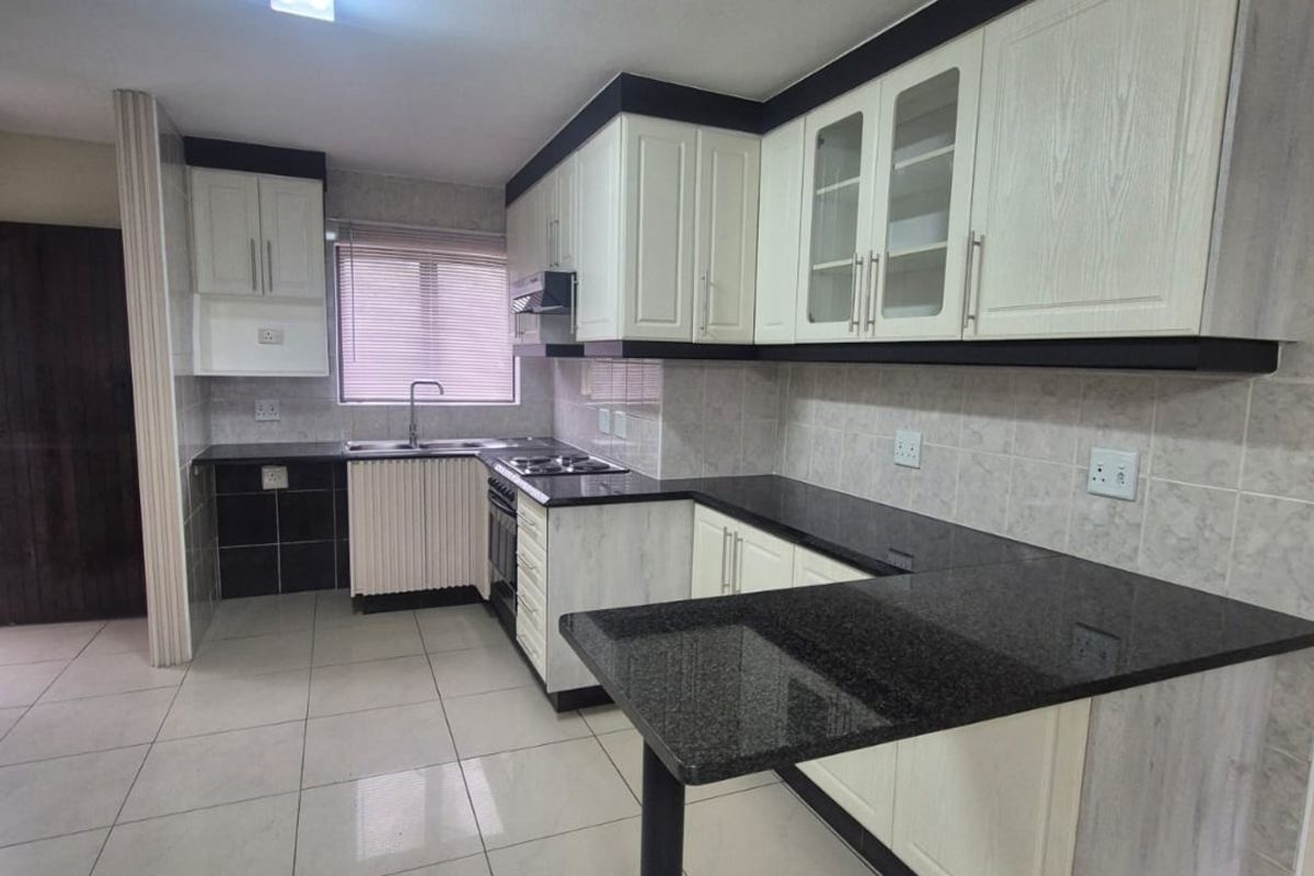 A clean, functional kitchen featuring granite countertops, ample built-in cabinetry, a breakfast bar, and tiled flooring, offering a neutral and well-maintained workspace.