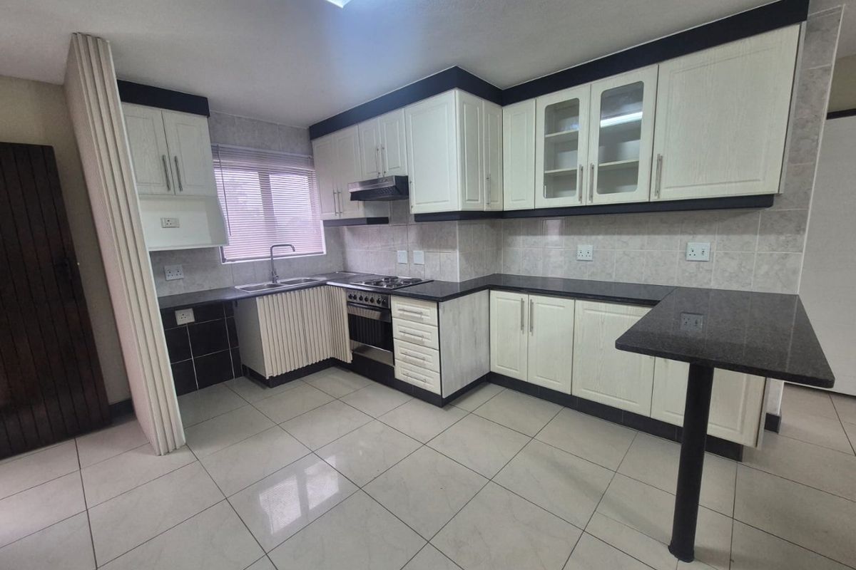 A clean, well-maintained kitchen featuring white cabinetry, dark granite countertops, a breakfast bar, and built-in appliances with neutral tiled flooring.