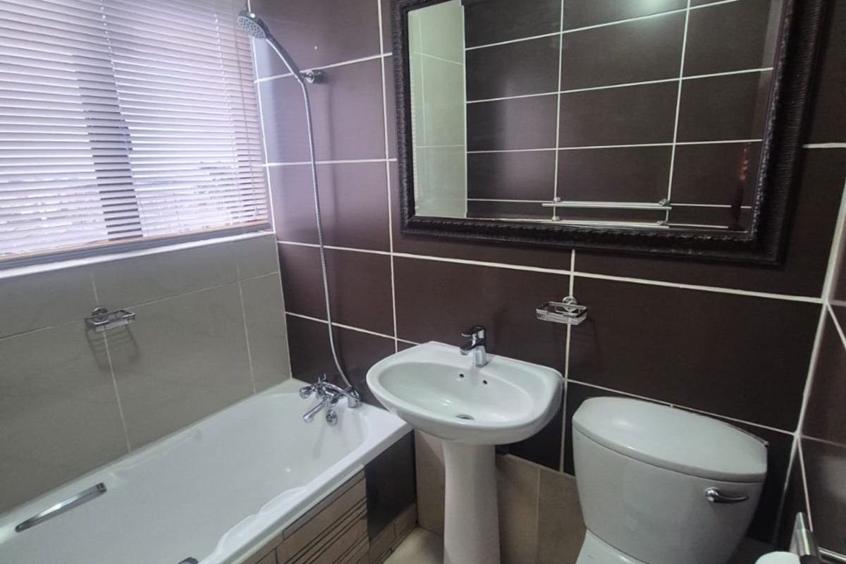 A functional bathroom featuring a pedestal basin, bathtub with shower mixer, and toilet, finished with dark brown and neutral wall tiling.