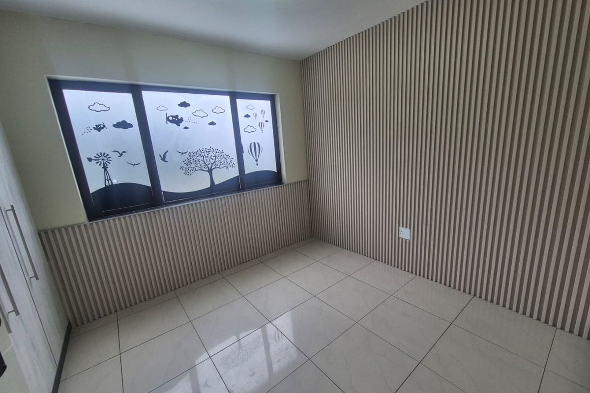 An empty bedroom featuring modern slatted wood wall paneling, neutral tiled flooring, and a built-in cupboard, offering a clean and contemporary living space.