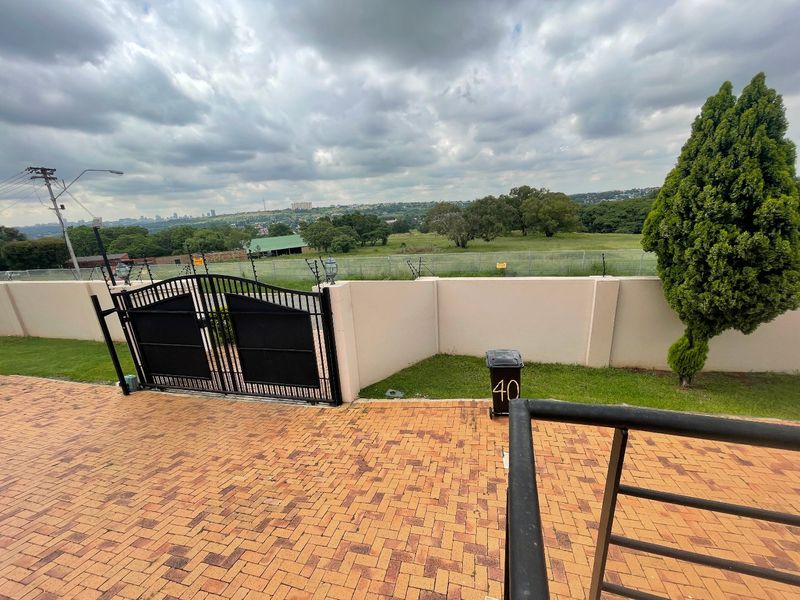 Front entrance area featuring a brick paved driveway, secure metal gate, and perimeter wall with electric fencing, overlooking a scenic landscape.