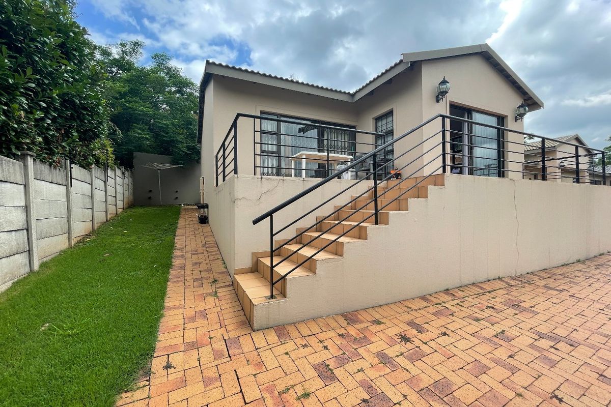 Rear view of the townhouse featuring a paved patio area, tiled staircase with metal railings, and sliding glass doors leading into the home.