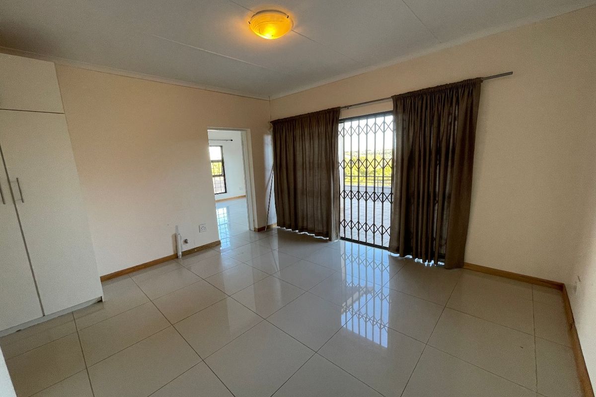 A spacious, empty bedroom featuring neutral tiled flooring, built-in cupboards, and a security gate leading to an outdoor area.