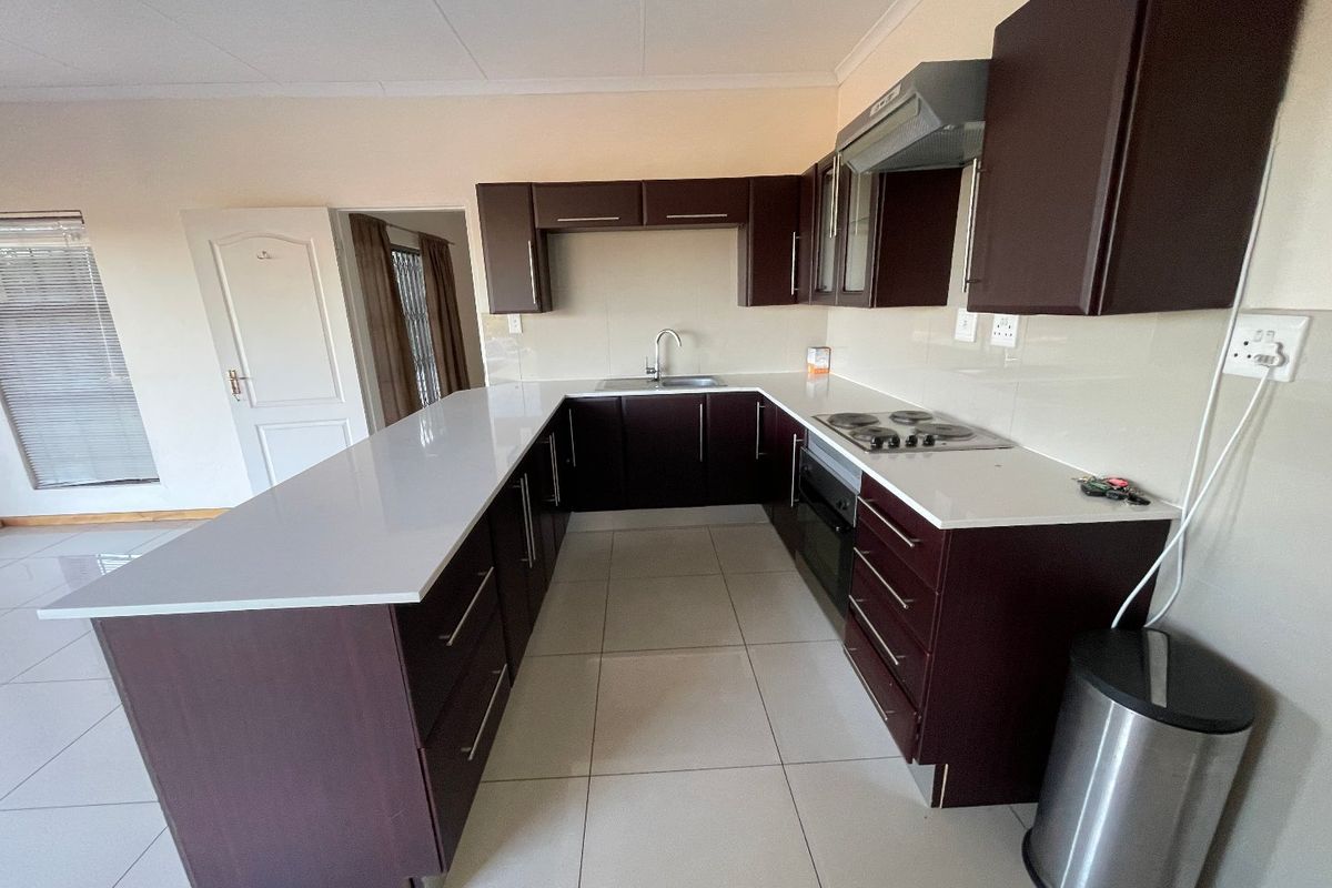 A modern U-shaped kitchen featuring dark cabinetry, stone countertops, built-in oven, electric hob, and tiled flooring in an open-plan layout.