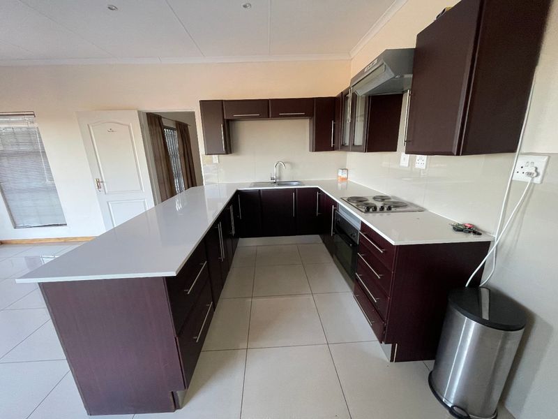 A modern U-shaped kitchen featuring dark cabinetry, stone countertops, built-in oven, electric hob, and tiled flooring in an open-plan layout.