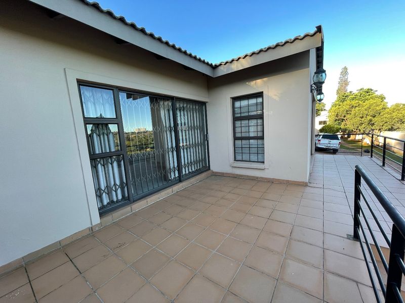 A spacious tiled patio area featuring sliding glass doors with security gates, external wall lighting, and metal safety railings.