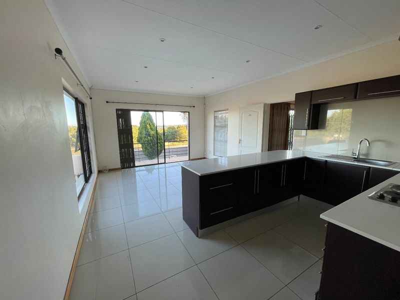Spacious open-plan living area featuring a modern kitchen with dark cabinetry, stone countertops, and tiled flooring, leading to a balcony with scenic views.
