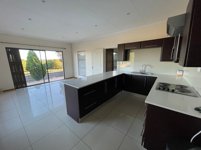 Spacious open-plan kitchen and living area featuring modern dark cabinetry, stone countertops, tiled flooring, and large sliding doors leading to an outdoor balcony.
