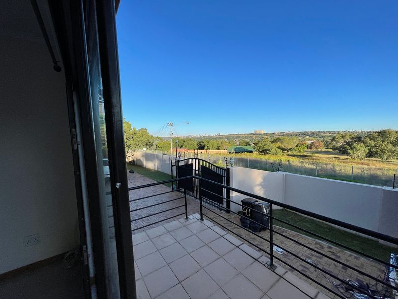 A tiled balcony overlooking a paved driveway, perimeter wall, and expansive suburban landscape views.