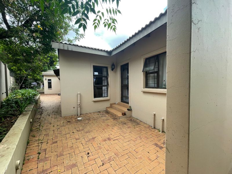 Rear exterior view of the townhouse featuring brick paving, a small set of tiled steps, and security-fitted windows.