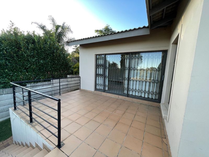 An elevated outdoor patio featuring tiled flooring, a metal safety balustrade, and sliding glass doors with security gates leading into the home.