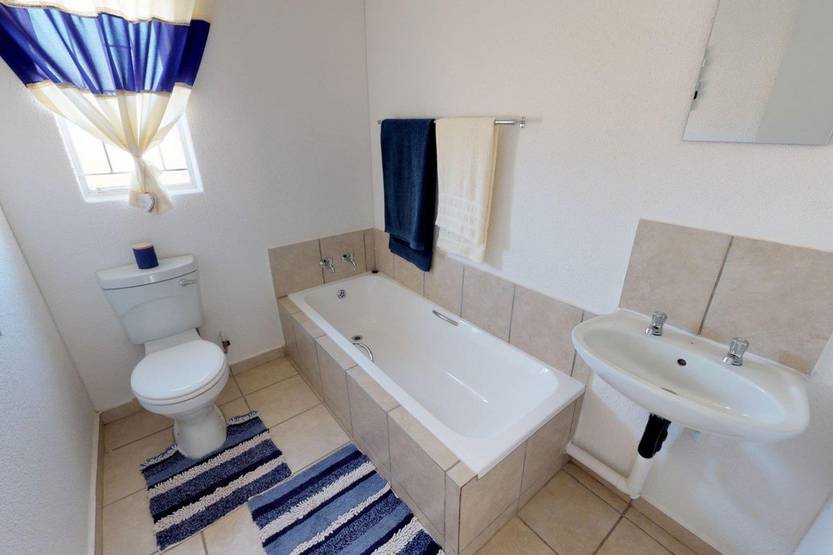 A functional bathroom featuring a built-in bathtub, pedestal washbasin, and toilet with neutral tiled flooring and splashbacks.