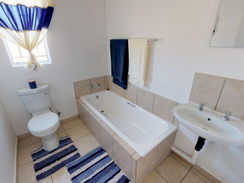 A functional bathroom featuring a built-in bathtub, pedestal washbasin, and toilet with neutral tiled flooring and splashbacks.