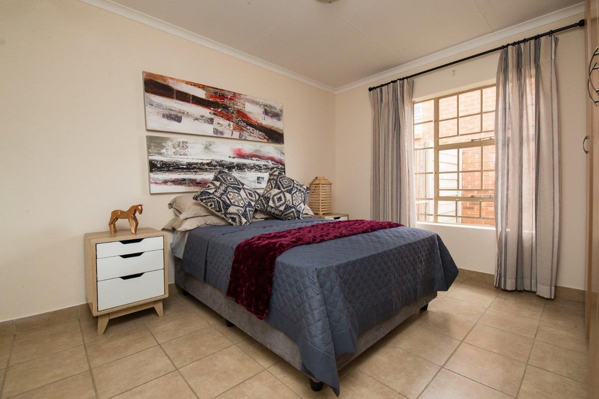 A well-maintained bedroom featuring tiled flooring, a built-in cupboard, and a window fitted with security burglar bars.