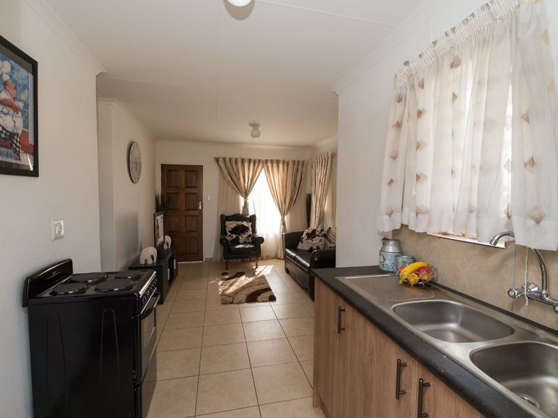 Open-plan living area featuring a functional kitchen with double sink and electric stove, flowing into a comfortable lounge space with tiled flooring throughout.
